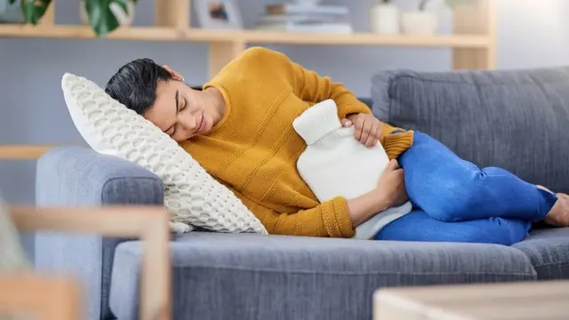 Mujer tumbada en un sofá con dolor abdominal.