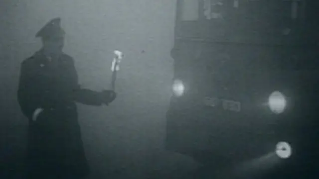 A policeman directs a bus with a flame during the Great Smog