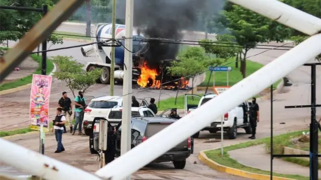 Hombres armados junto a un vehículo incendiado