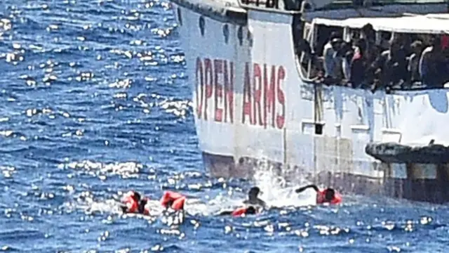 Migrants in water next to Open Arms rescue ship