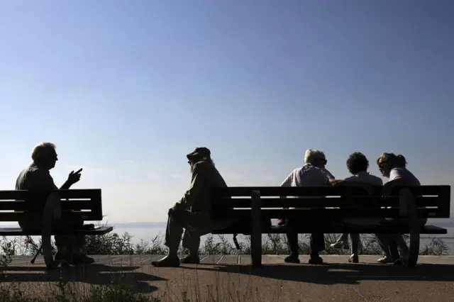 Ancianos sentados en dos bancos en Italia.
