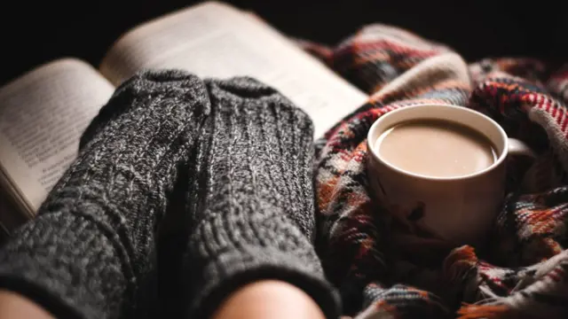 Libro, taza de café y pies con medias