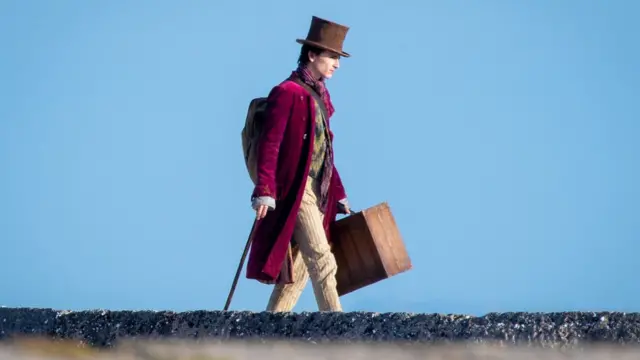 Timothée Chalamet como Willy Wonka, uma homem brancojogo da roleta no bet365casaco vinho, cachecol, bengala na mão e chapéu