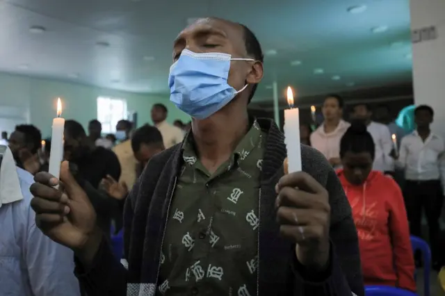 A man holds candles as he and others pray.