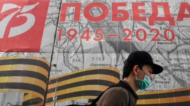 شاب يرتدي قناع يمر بجوار ملصق دعائي