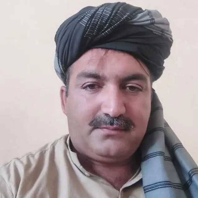 د ملک طارق وزیر عکس دی چې لونګۍ یې پر سر ده، ږیره یې خرېیلې او غټ بریتونه لري، پيکه کریمي رنګ کمیس یې اغوستی.