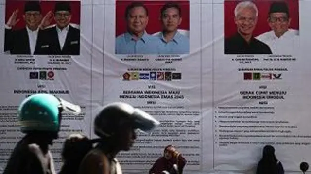 Warga duduk di dekat baliho sosialisasi tiga pasangan Calon Presiden dan Wakil Presiden 2024 yang terpajang di Pasar Barito, Kota Ternate, Maluku Utara, Kamis (14/12/2023).