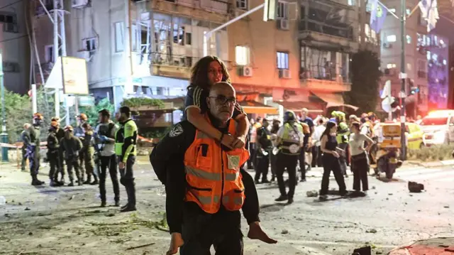 Tel Aviv yakınlarındaki Ramat Gan'da İran'dan atılan bir füzenin isabet ettiği bölgede yaralı bir kızı sırtında taşıyan bir kurtarma görevlisi görülüyor.