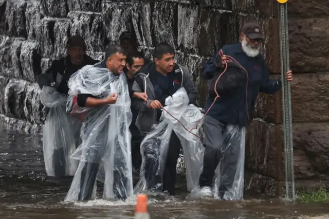 Seis homens com capasbetfair ao vivo flamengochuva atravessam rua alagada