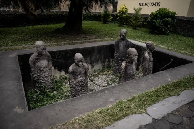 Des pierres taillées en formes humaines avec des chaînes au cou symbolisant comment les esclaves étaient traités à Zanzibar.