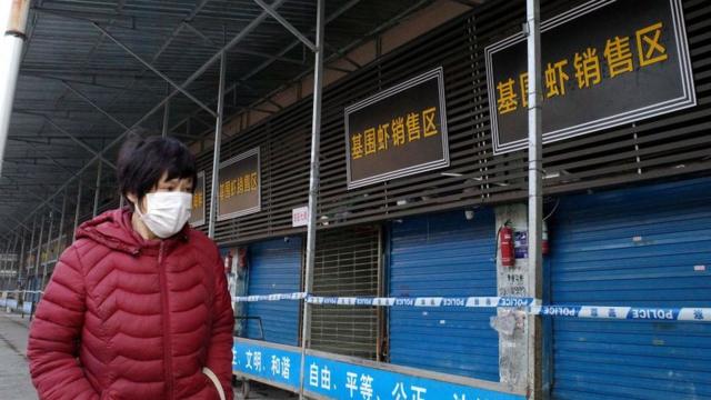Una mujer usando una mascarilla camina cerca de un mercado cerrado en China.