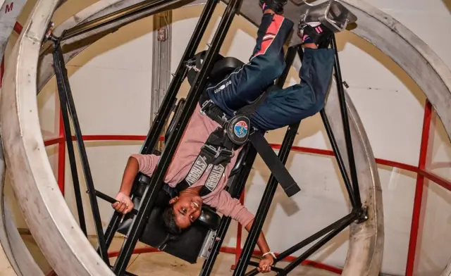 Sandali Kumarasing held upside down while strapped into a spinning device to simulate weightlessness at Space Camp