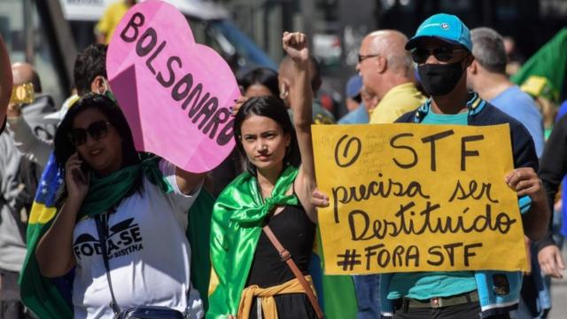 Três manifestantes em rua segurando cartaz em formato de coração dizendo 'Bolsonaro' e outro 'O STF precisa ser destituído'