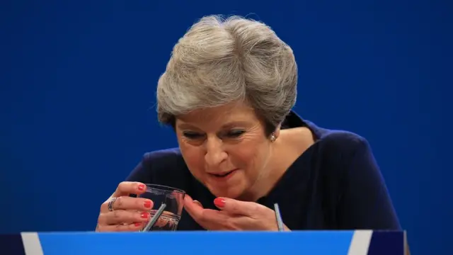 Theresa May tossindo tomando um copo d'água