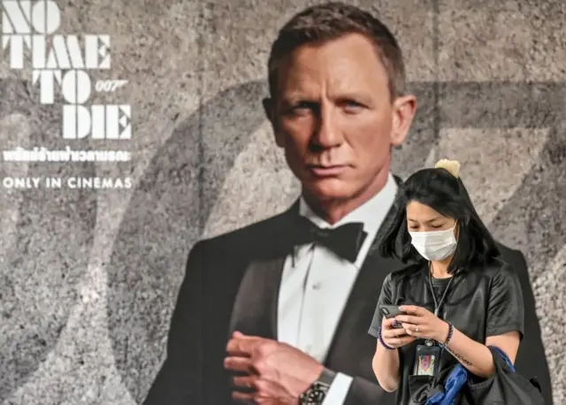 Женщина в маске на фоне постера к новому фильму Джеймса Бонда