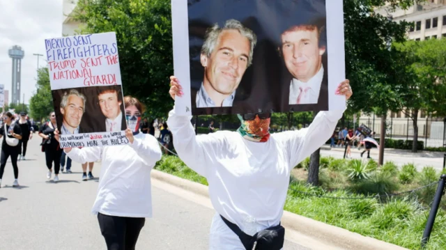 امرأتان ملثمتان ترفعان لافتة عليها صورة تجمع ترامب وإبستين