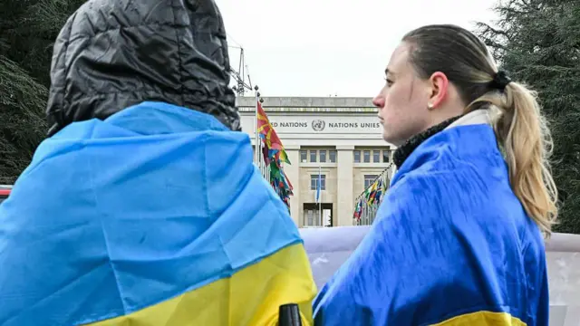 Protesters wearing Ukrainian flags stand outside the United Nations office as a new round of talks between Russian, Ukrainian and US negotiators aimed at finding a solution to four years of fighting in Ukraine takes place in Geneva in February 2026 