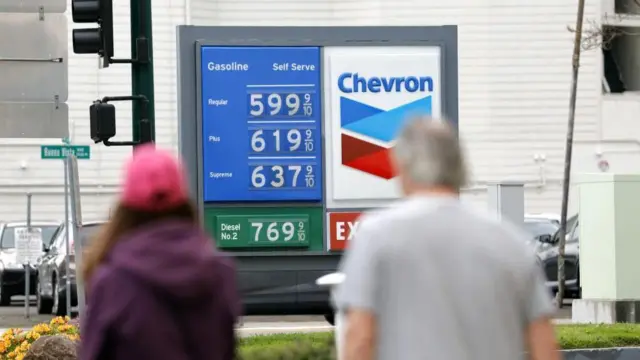 ガソリンスタンドに表示されている価格を、歩道から男女が見ている