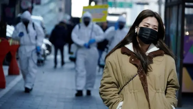A woman wearing a mask as a preventive measure against the coronavirus walks past South Korean soldiers in protective gear sanitizing a street in Seoul