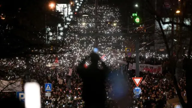 Seorang pria mengambil foto ribuan mahasiswa dan warga yang menghadiri protes atas runtuhnya atap stasiun kereta api yang menewaskan 15 orang bulan lalu, di tengah blokade yang meluas terhadap institusi pendidikan tinggi di pusat kota Beograd pada 22 Desember 2024.