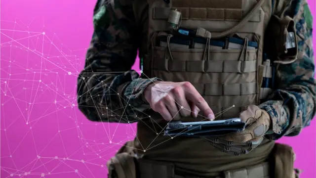 A photo illustration shows a man in combat fatigues tapping on a tablet, from which flows an abstract representation of data into the pink background
