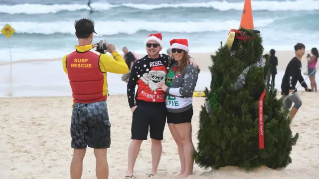 A Surf Life Saver takes a picture of a couple in front of a Christmas Tree on Bondi Beach in Sydney