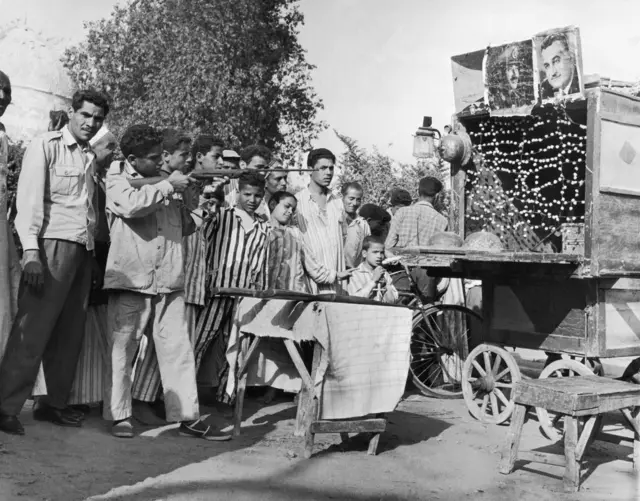 شباب يمارسون الرماية أو "النشان" بالبندقية تجاه لوح مليء بالمفرقعات الصغيرة، خلال احتفالات المولد النبوي الشريف في مصر في خمسينيات القرن الماضي