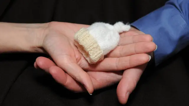 Manos de padres sosteniendo gorro de bebé