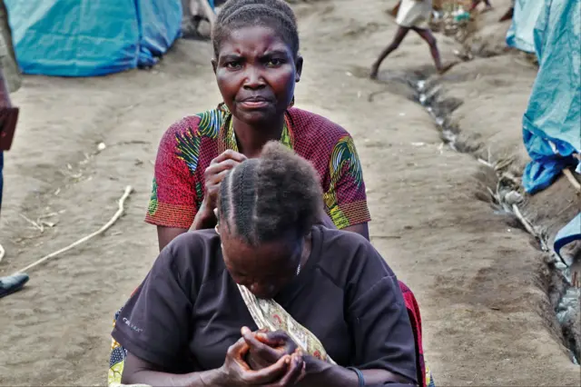 La vie continue dans le camp juste à côté une femme fait des tresses à sa voisine.