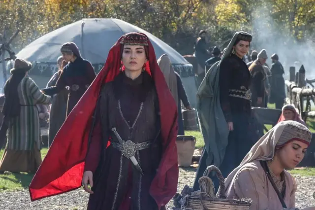 Diziden bir kare, çadırların önünde yürüyen bir kadın