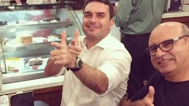 Flávio Bolsonaro e Queiroz posam para foto fazendo sinalbet cadastroarma com os dedos