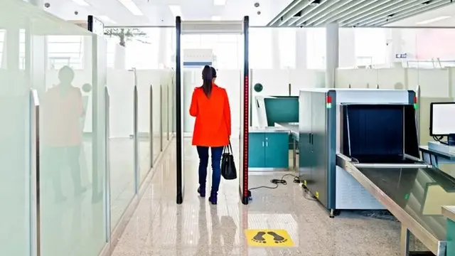 Una mujer pasa por debajo de un arco de seguridad en el aeropuerto.