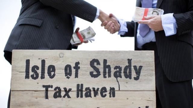 Unseen protestors dressed as a businessman shake hands whilst holding wads of fake currency on a protest site named by participants as the "Isle of Shady Tax Haven Poor people keep out!" in London on June 14, 2013,
