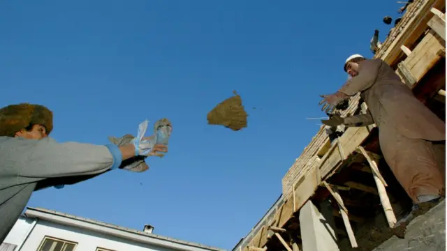 Pekerja konstruksi Afghanistan melemparkan lumpur ke atap yang sedang dibangun di Rumah Sakit Wanita Rabia Balkhi 30 Januari 2003 di Kabul, Afghanistan.