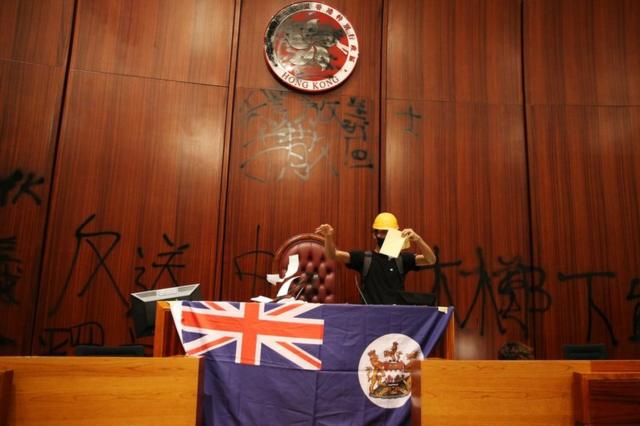 示威者在香港立法会会议厅涂污区徽，展示港英旗帜。