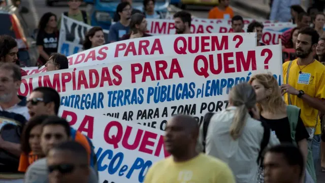 Manifestantes com cartaz dizendo "Olimpíadas para quem?"
