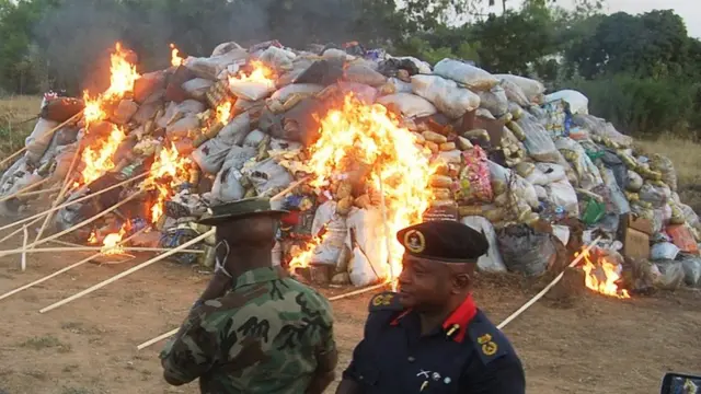 one soldier and one civil defence NDLEA dey watch as hard drugs dey burn.