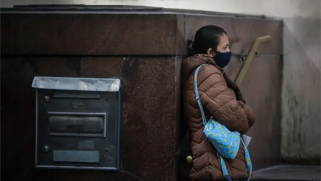 Mulhermáscara parada na rua, encostadauma parede