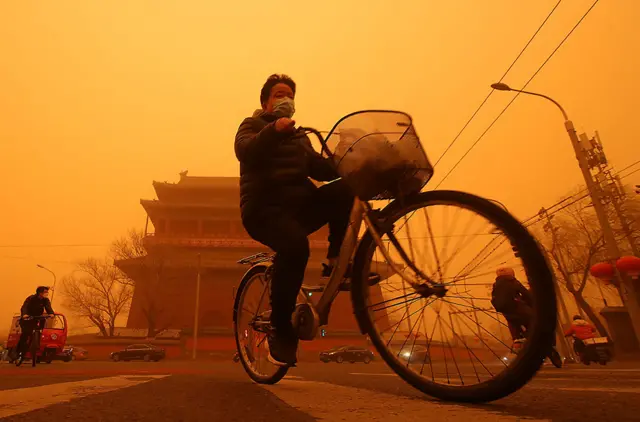 A cyclist passes a temple whilst surrounded by a thick sandstorm