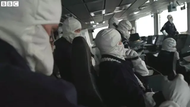 Ці білі маски та рукавиці - захисне спорядження (так зване anti-flash gear) британських моряків на випадок пожежі. Скріншот з репортажу кореспондента BBC Джонатана Біла