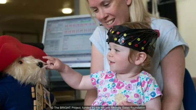 Mulher segura bebê com capacete futurista