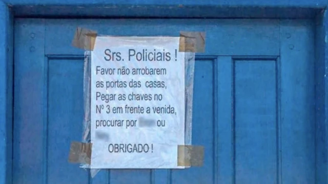 Imagem mostra porta azulcasa com aviso que diz: 'srs. policias! Favor não arrombarem as portas das casas, pegar as chaves no no. 3frente à avenida, procurar por (ilegível) ou (ilegível), obrigado!'