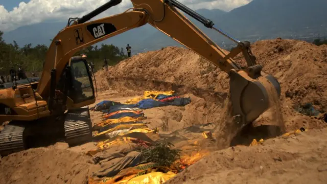 Petugas dengan alat berat mengubur jenazah korban gempa Palu di TPU Poboya Indah, Palu, Sulawesi Tengah, Selasa (2/10).