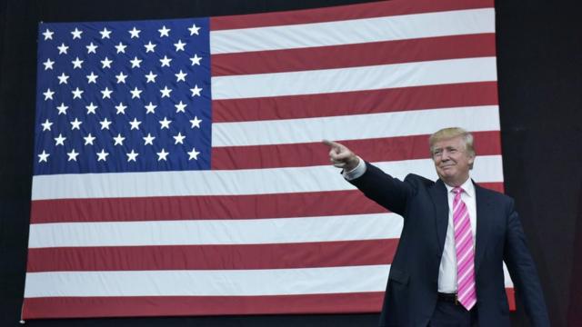 Donald Trump points in front of an American flag