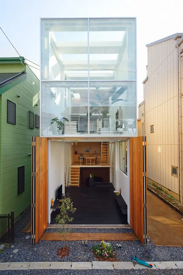Casa estrecha de diseño contemporáneo con fachada acristalada de doble altura y amplias puertas abatibles de madera abiertas al exterior.