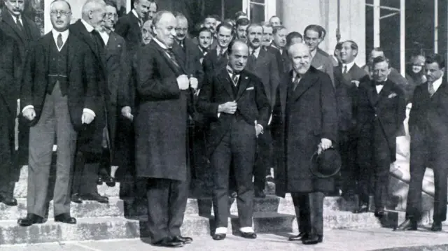 İtilaf Devletleri baş diplomatları Lozan'daki bir otelin önünde poz veriyor. Siyah beyaz fotoğraftaki herkes erkek ve üzerlerinde takım elbise var.