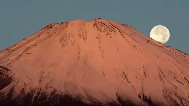 Luna se esconde detrás de una montaña nevada.