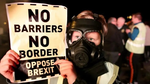 Manifestante anti-Brexit com máscaragás segura uma placa que diz: 'sem barreiras, sem fronteiras'