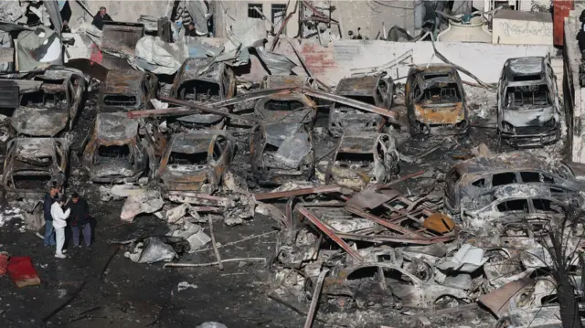 在贝鲁特滨海大道(Corniche el-Mazraa)街区,人们走过以色列空袭摧毁的汽车和建筑物废墟。