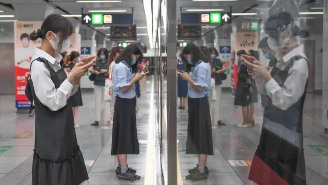 Passengers look at their smartphones as they wait for a subway train at a subway station on April 27, 2021 in Hangzhou